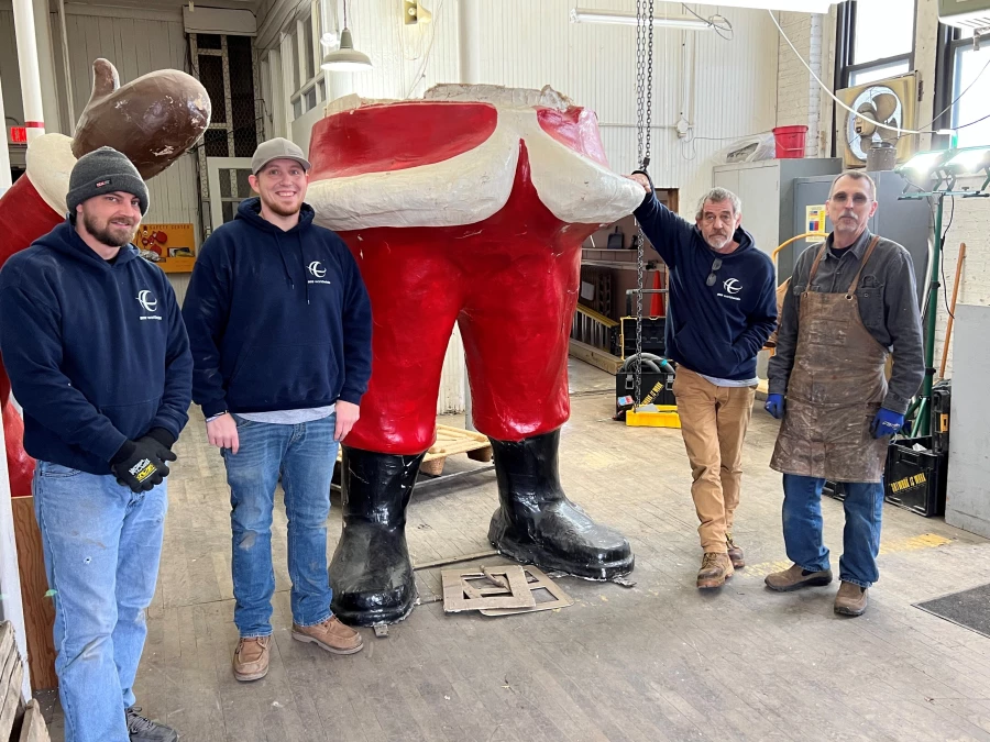 Four men with facial hair stand on both sides of the lower half of a santa statue.