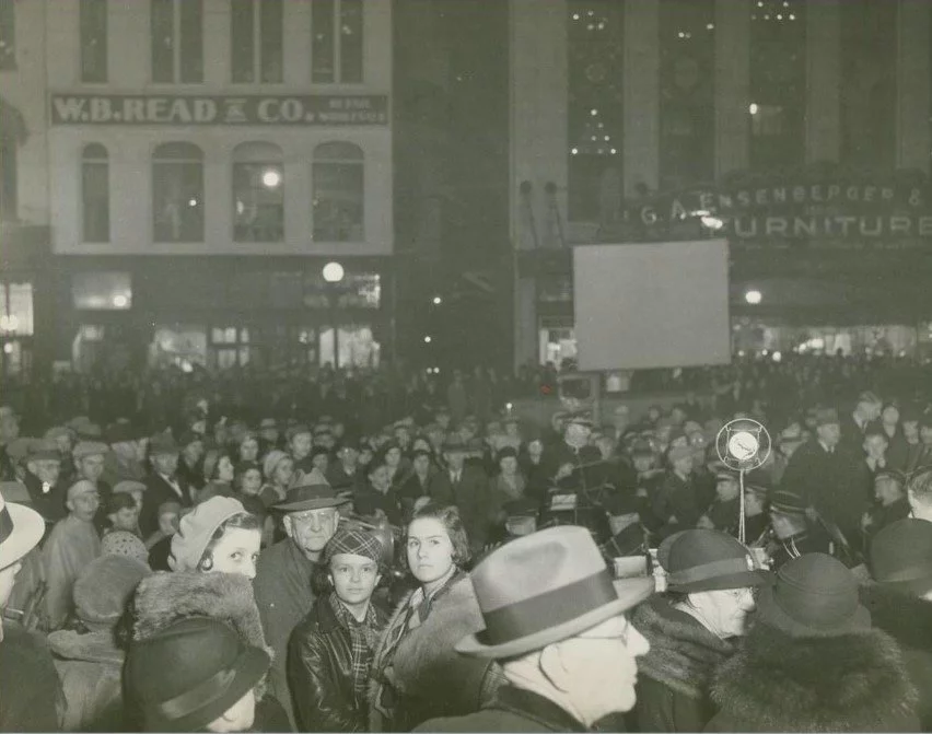 a large crowd is seen in front of Ensenberger Furniture store and the W.B.READ & CO buildings.