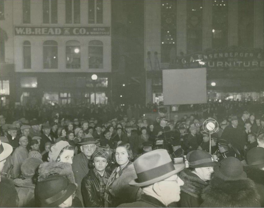a large crowd is seen in front of Ensenberger Furniture store and the W.B.READ & CO buildings.