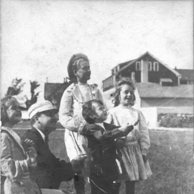 A boy flys a kite, surrounded by two young girls, an older woman, and a man in a hat.