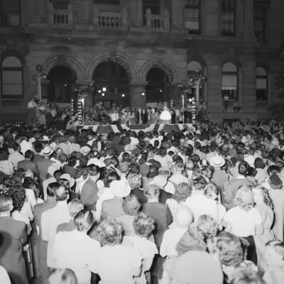 A crowd dressed in white stands in front of a stage in front of a historic courthouse