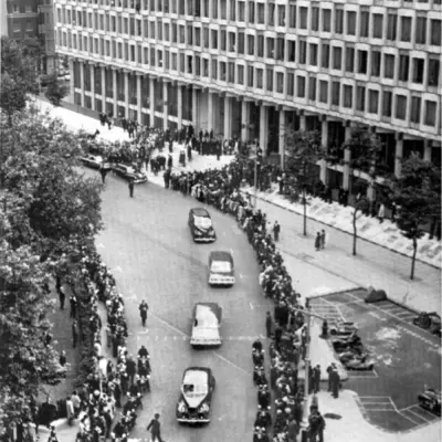 People dressed in black line the street as a line of black cars move toward the viewer.