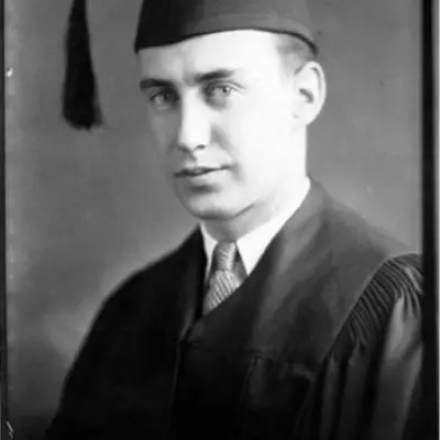 A man dressed in university robes poses for a portrait.