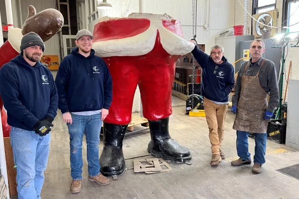 Four men with facial hair stand on both sides of the lower half of a santa statue.