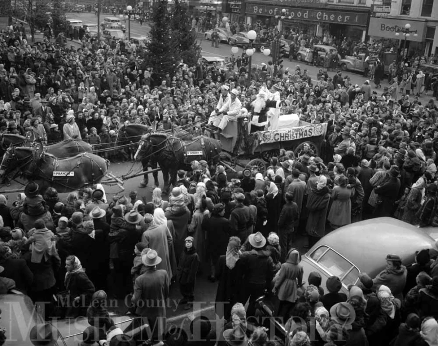 a crowd surrounds santa, who is on a wagon being pulled by 4 horses in Downtown Bloomington