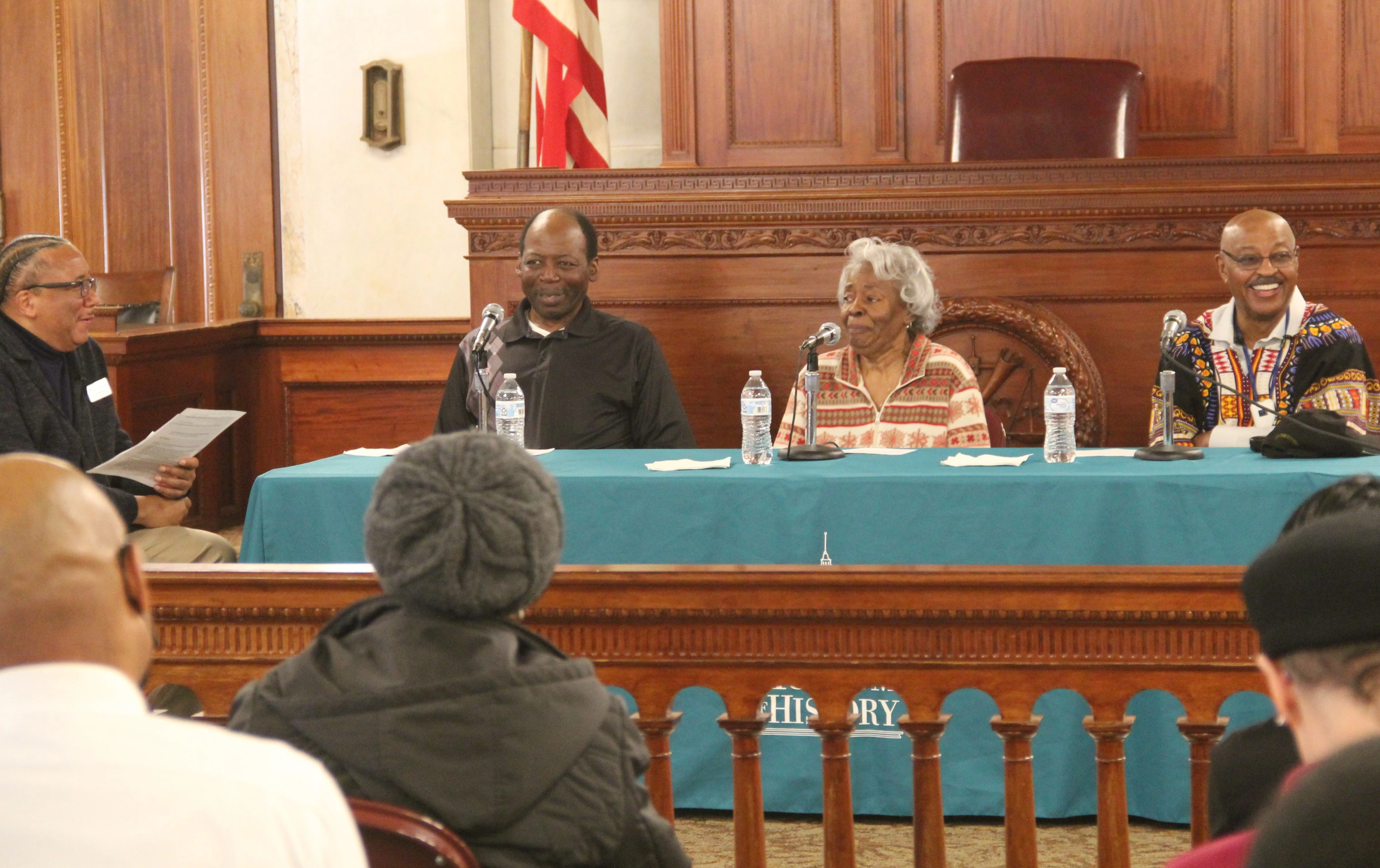 Three panelists and a moderator sit in front of a crowd in the Museum's courtroom