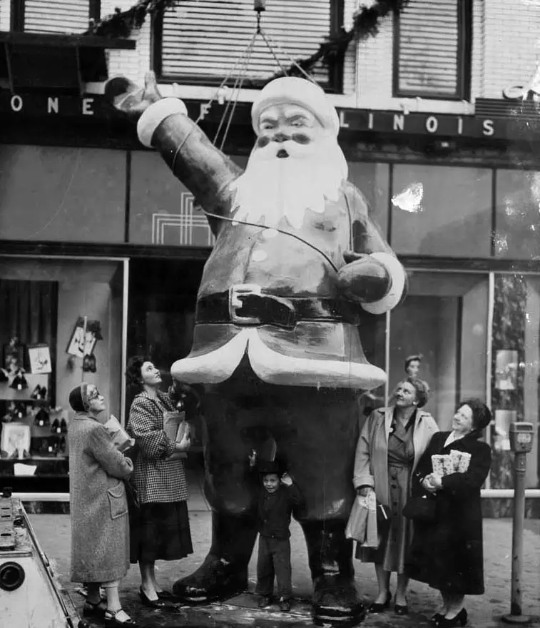 Livingston Santa on the sidewalk, four women standing and looking up at it.
