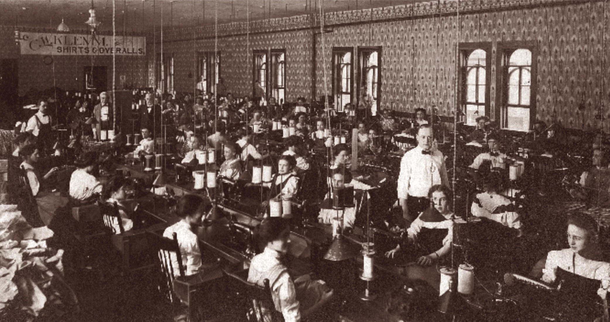interior factory photograph showing women at sowing machines and a man standing in the middle.