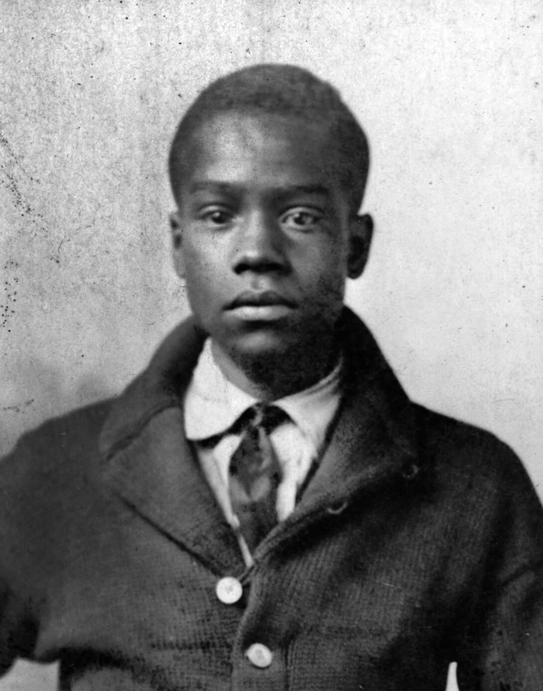Black and white portrait of a Black man in a white shirt, tie and dark jacket.