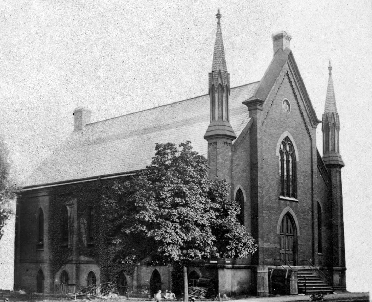 Black and white photo of a dark brick church with two steeples.