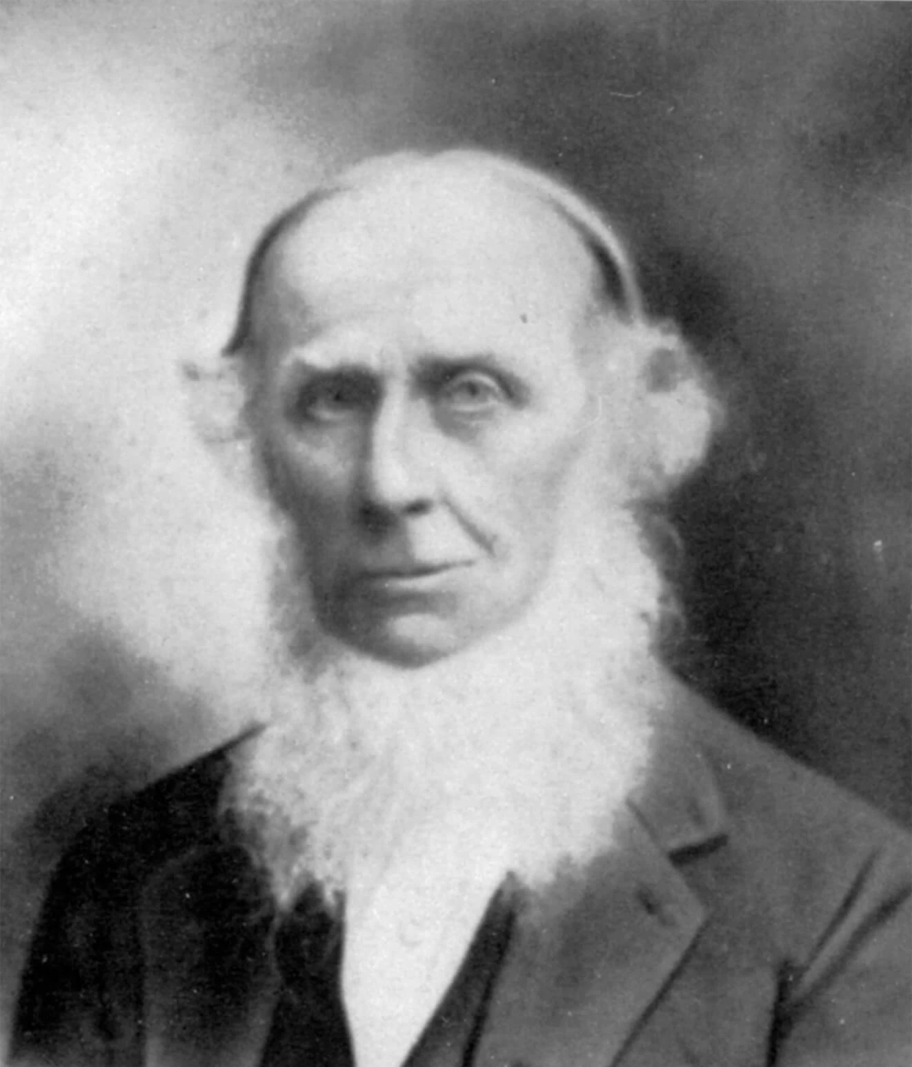 Portrait of Jonathan Yoder, a balding white man with a long white beard, stern face, and wearing a dark suit and vest with white shirt. His face is clean shaven all the way to the bottom edge of his jaw line, where his long beard begins,