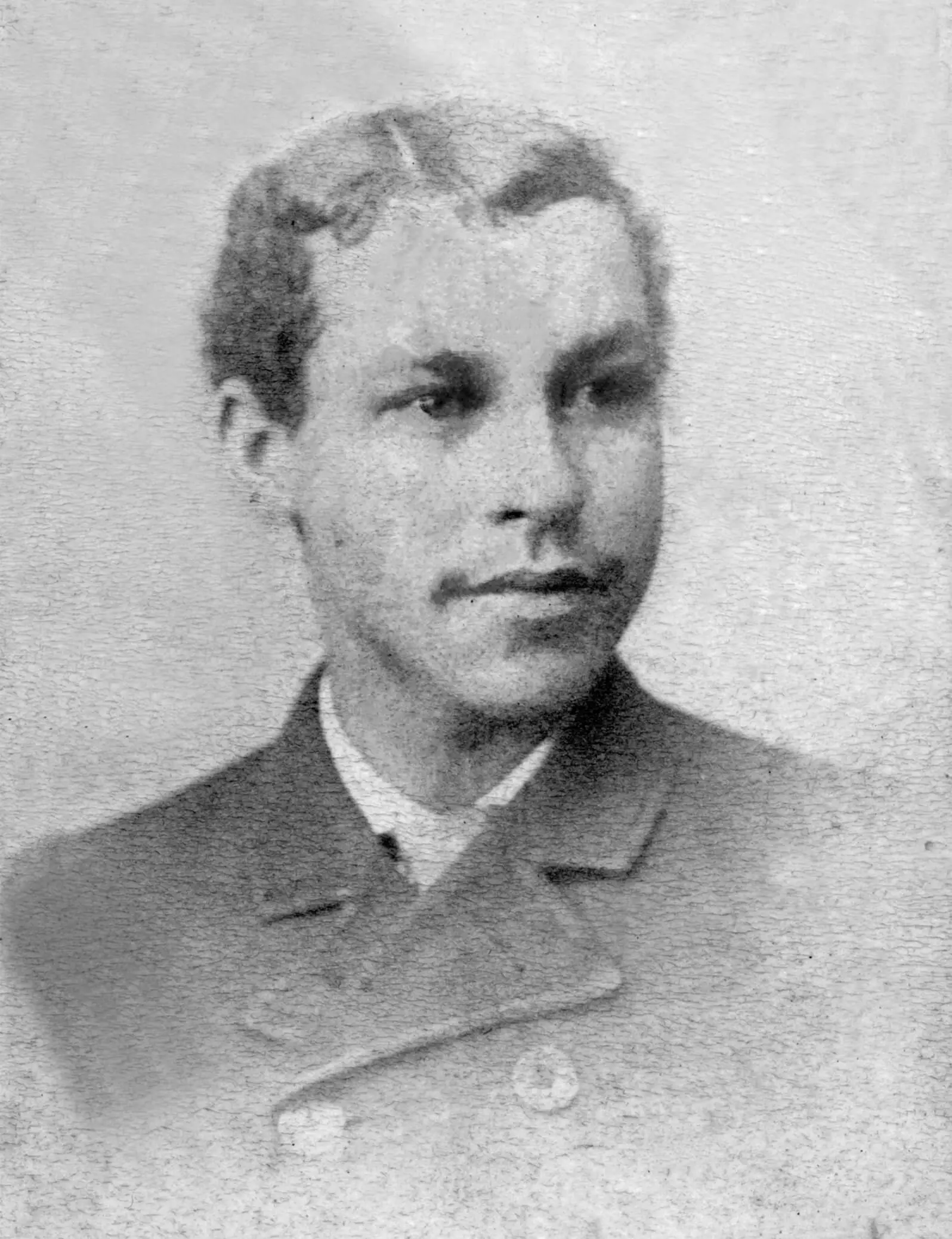 Photo of a young Black man with short dark hair and wearing a dark jacket, tie and collard shirt. There appear to be hints of a mustache at the corners of his lips. His hair is dark and wavy and parted on the side.