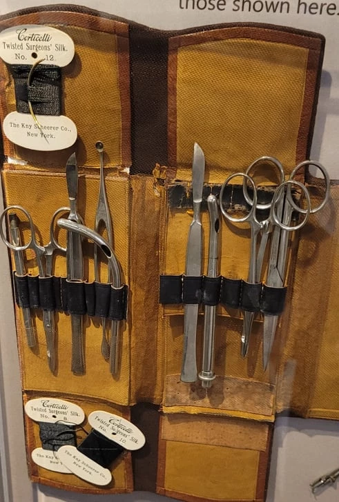 A surgical kit containing scalpels, scissors, probes, suture needles, and suture silk.