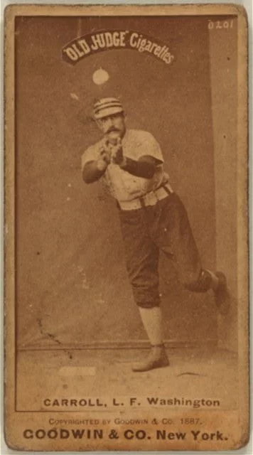 portrait of a man wearing a baseball uniform getting ready to catch a baseball. He has bare hands extended in front of him, and is leaning on his right leg, left leg bent in the air behind him.