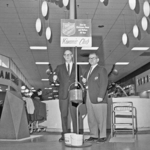 two men stand next to a pail, with a salvation army sign