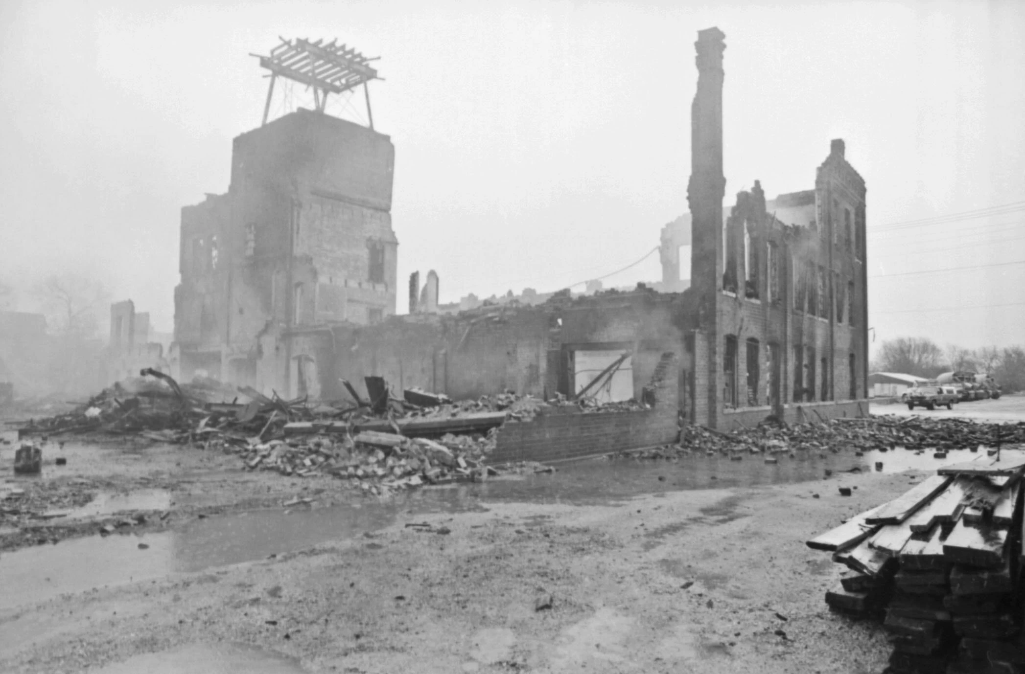 through the haze there is a crumbled brick building, some fascade still stands but most of the brick building is rubble on the ground.
