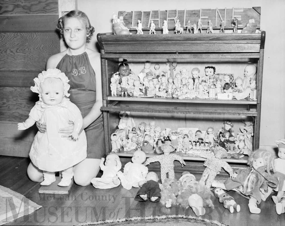 Young girl poses with doll collection, 1938.