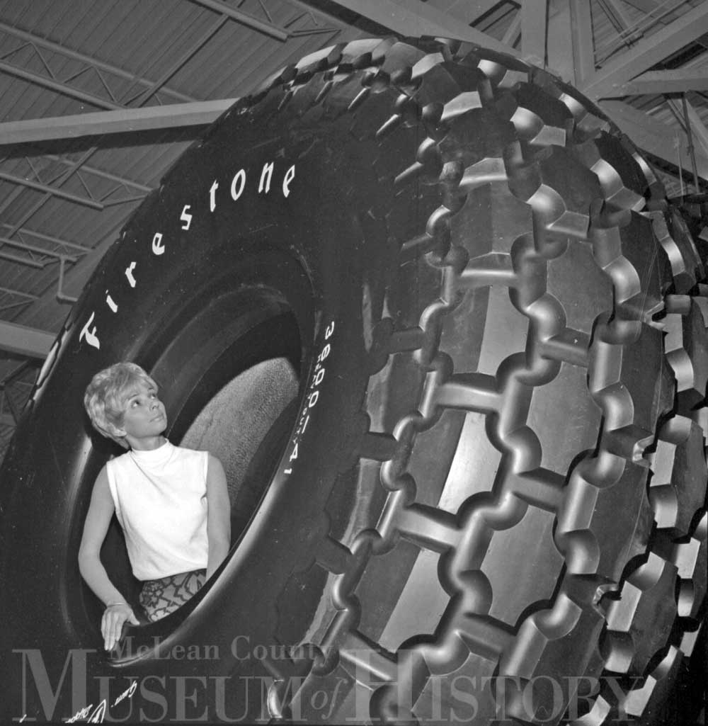 a woman is pictured standing in the middle of a gigantic approx 12 foot diameter firestone tire.