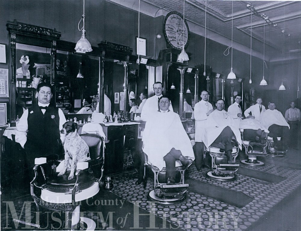 Group of men, and a dog, posing for a photo in a barbershop, 1914.