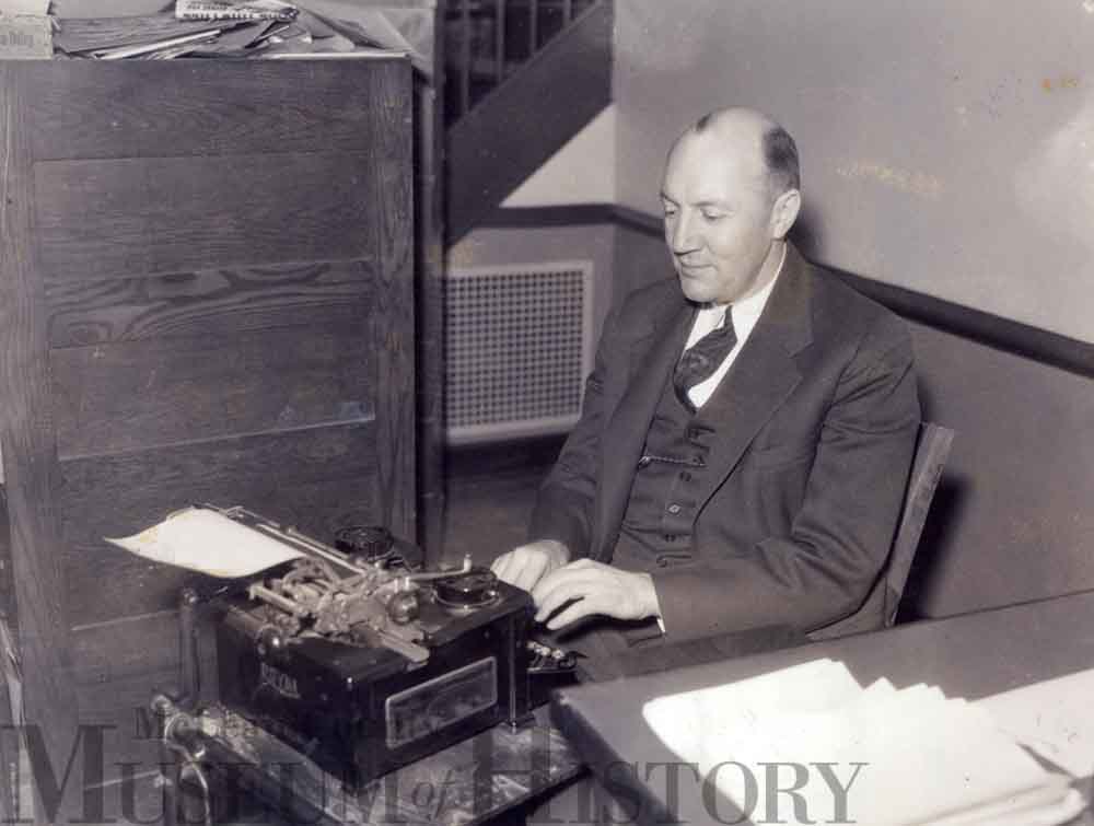 Pantagraph sports editor Fred “Brick” Young sitting at a desk typing on a typewriter